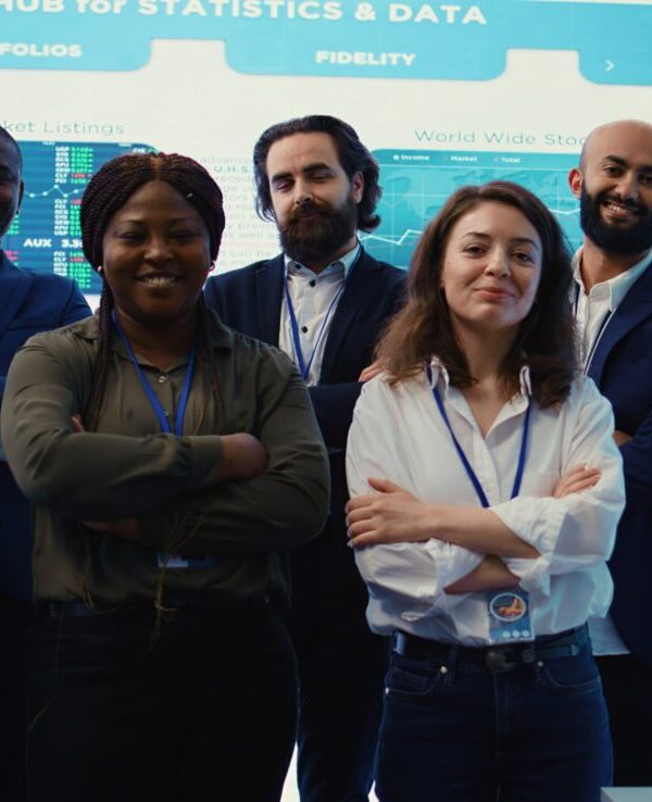 Diverse group of business professionals posing together in monitoring room, multinational company headquarters. Executive management team working with big data screen in the office. Camera B.
